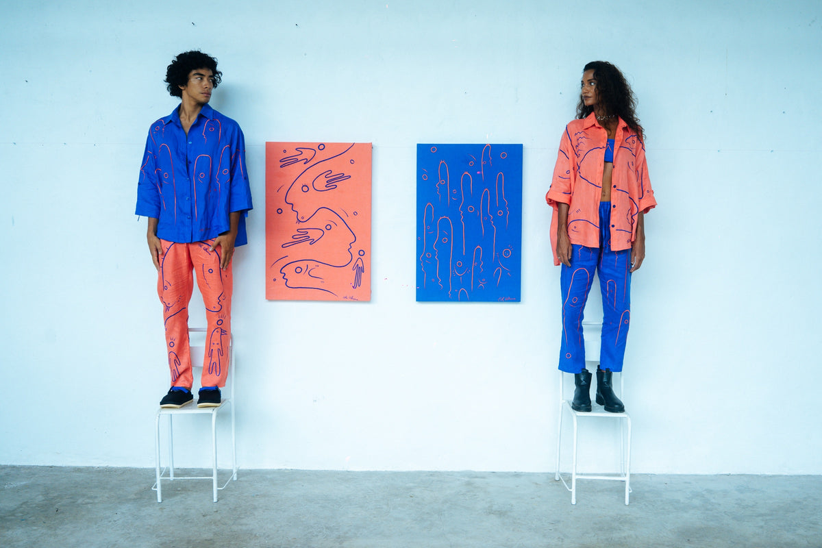 Two people wearing complementary UKENA linen sets beside two works on canvas