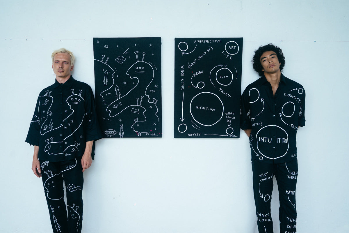Two people wearing black UKENA wearable artworks beside works on canvas
