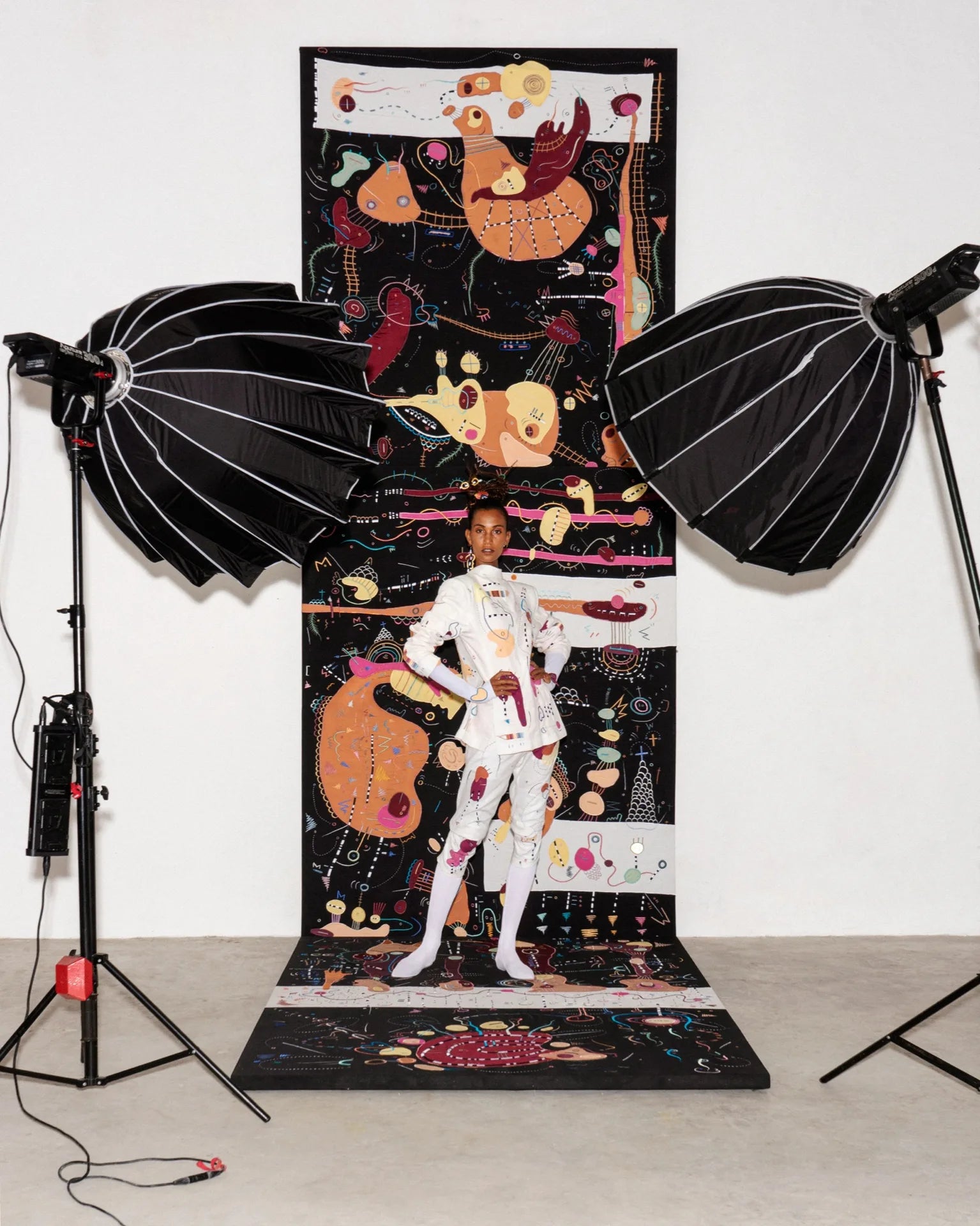 A white embroidered suit in front of a tall Antidote artwork during a campaign shoot