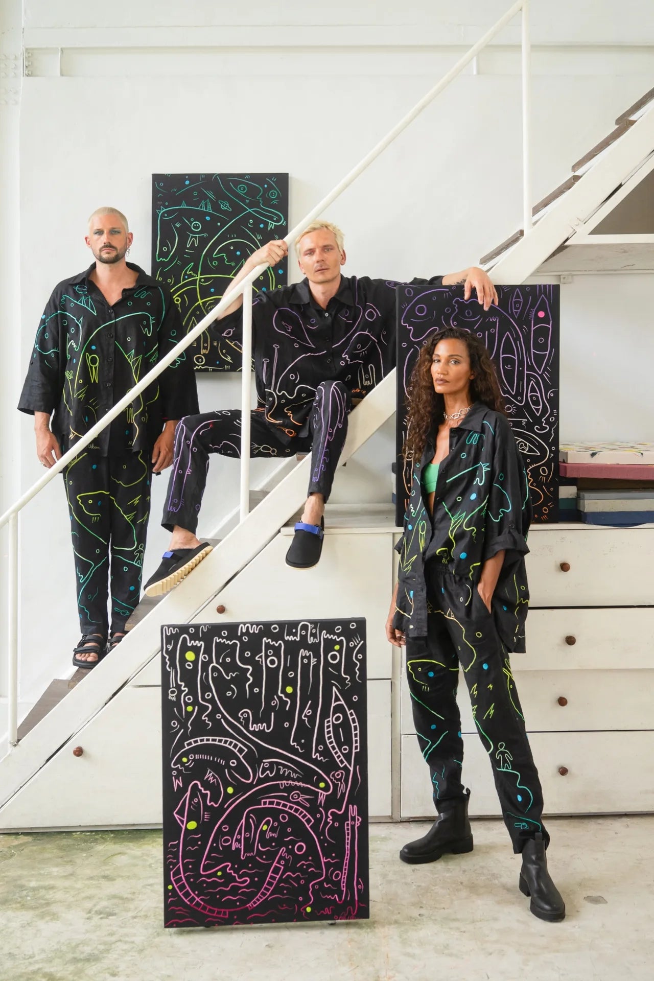 Three people wearing dark linen works beside related wall pieces