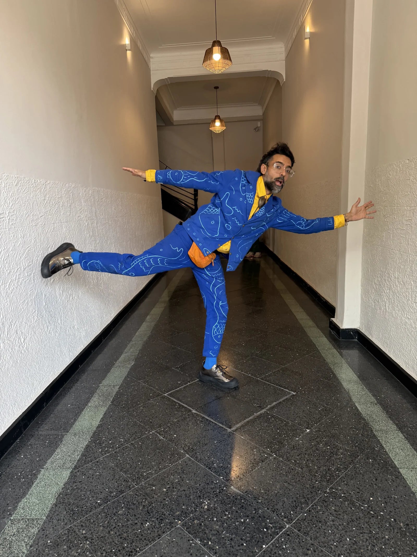 Varun balances playfully in a hallway wearing a blue embroidered suit