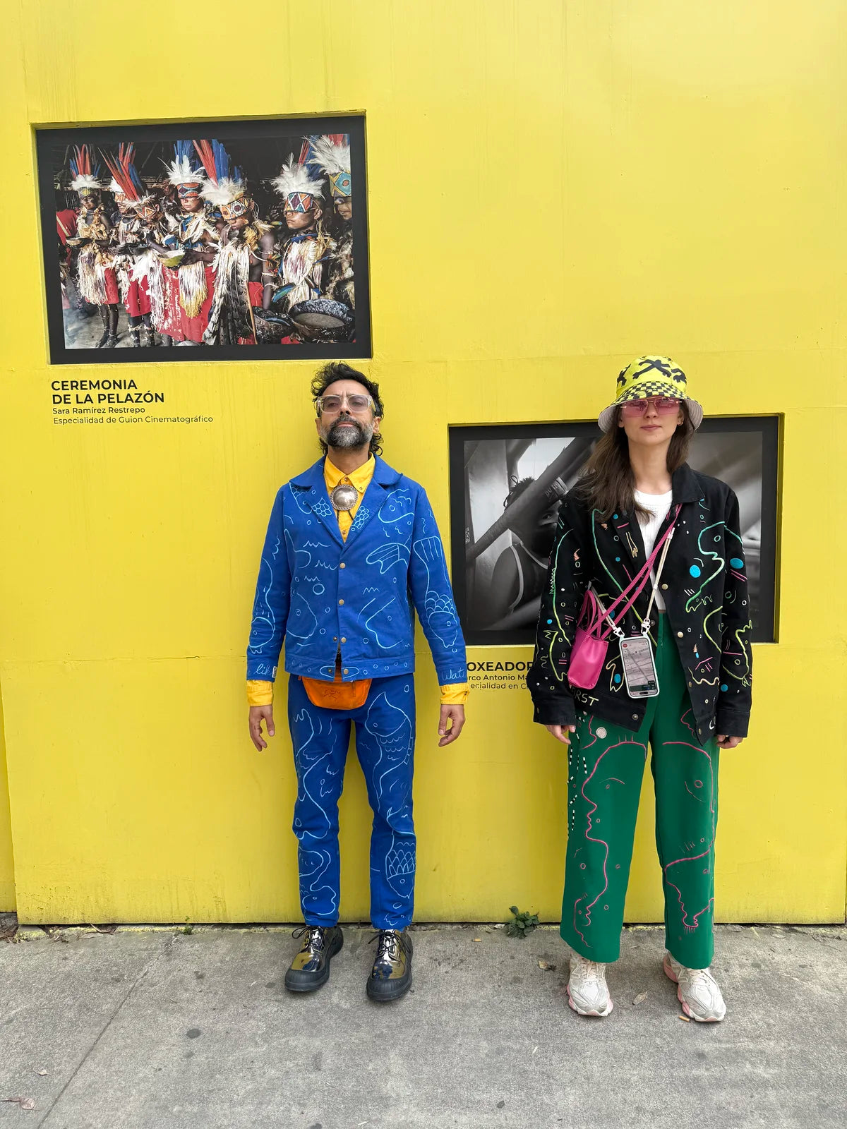 Varun and Morta in blue, black and green against the yellow wall