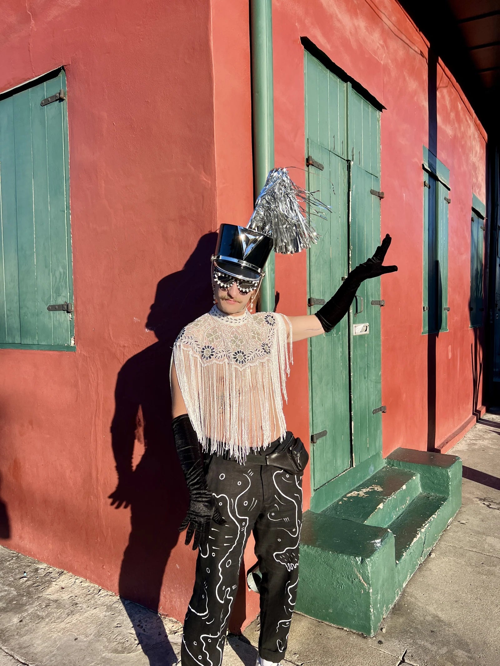 Forrest wears the embroidered trousers with a fringed top and hat beside green shutters