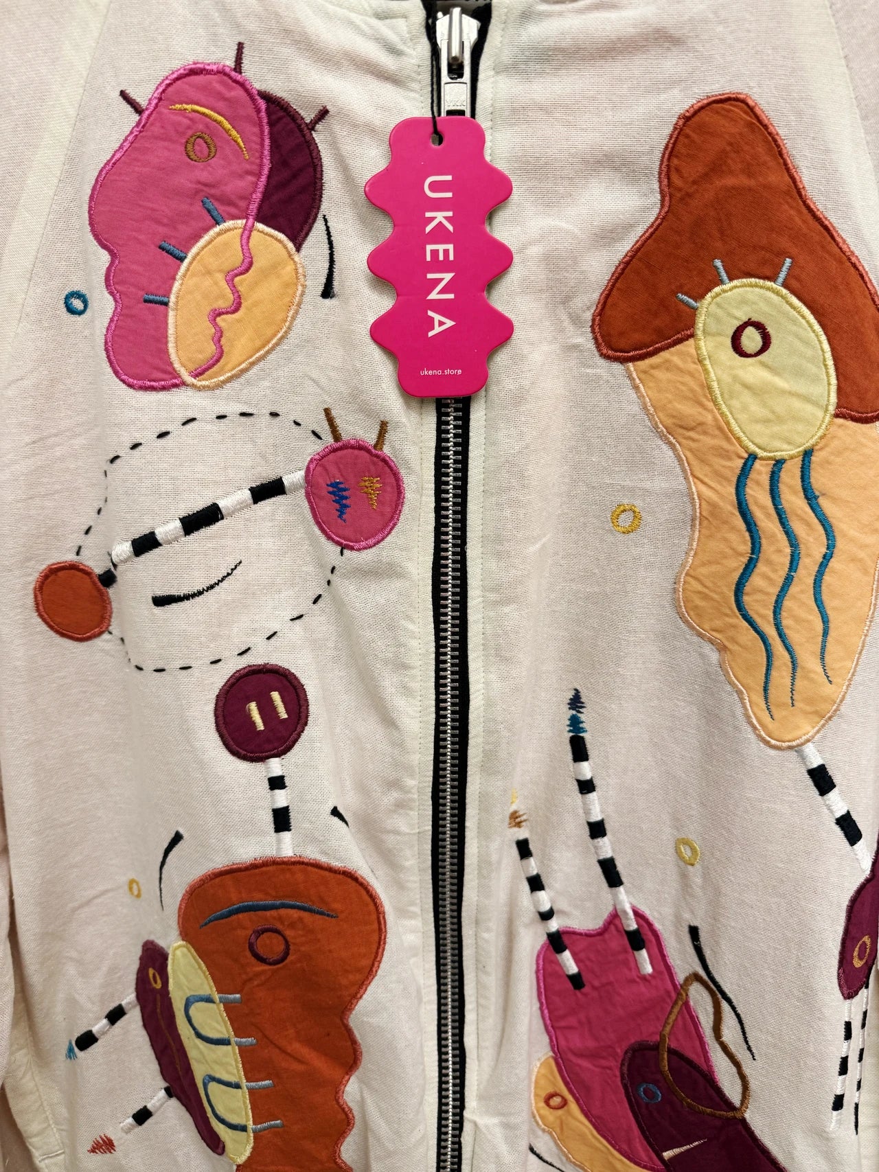 Embroidered figures and the UKENA tag on cream linen
