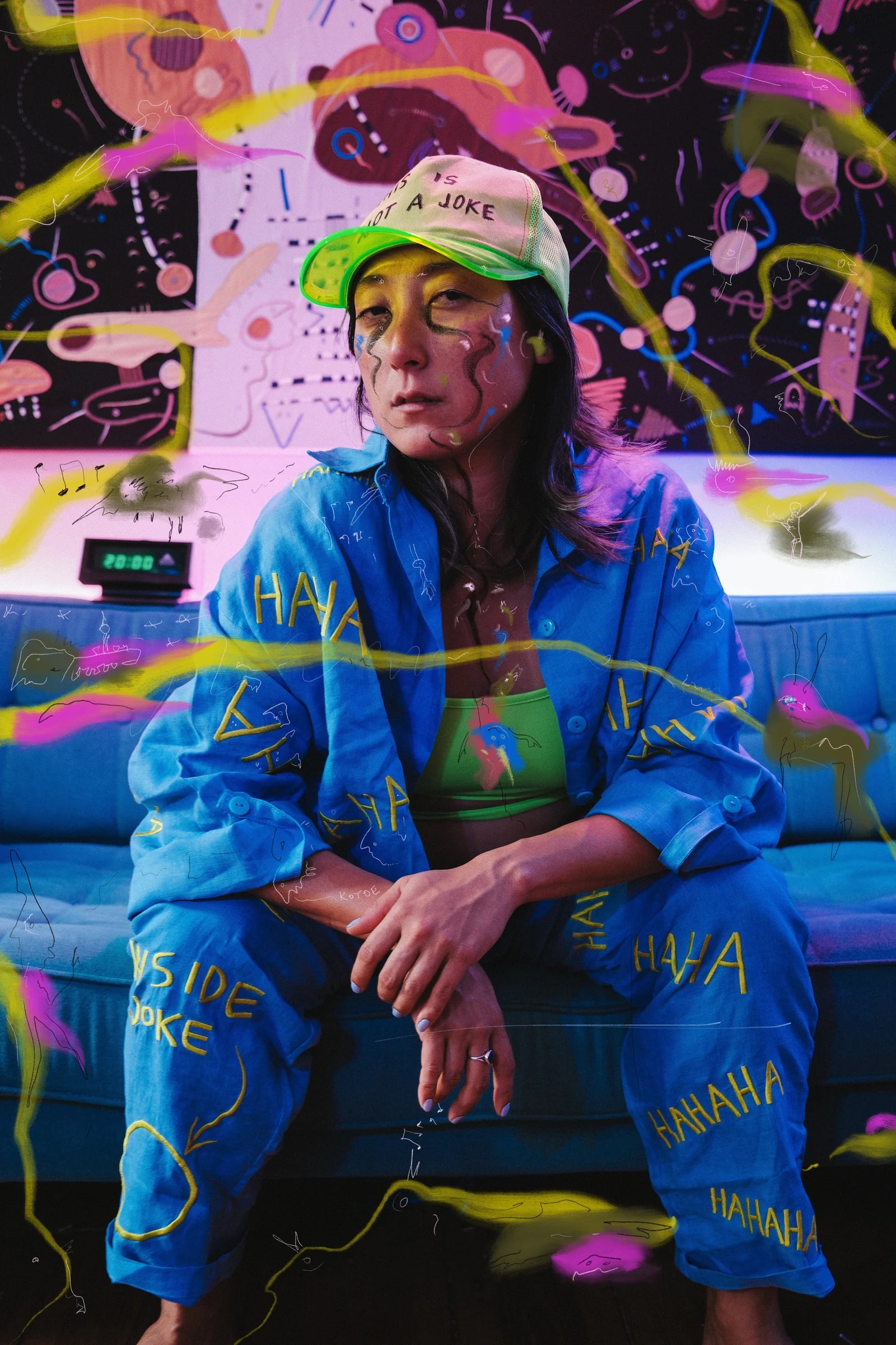 KOTOE seated in blue embroidered linen, surrounded by colourful drawings