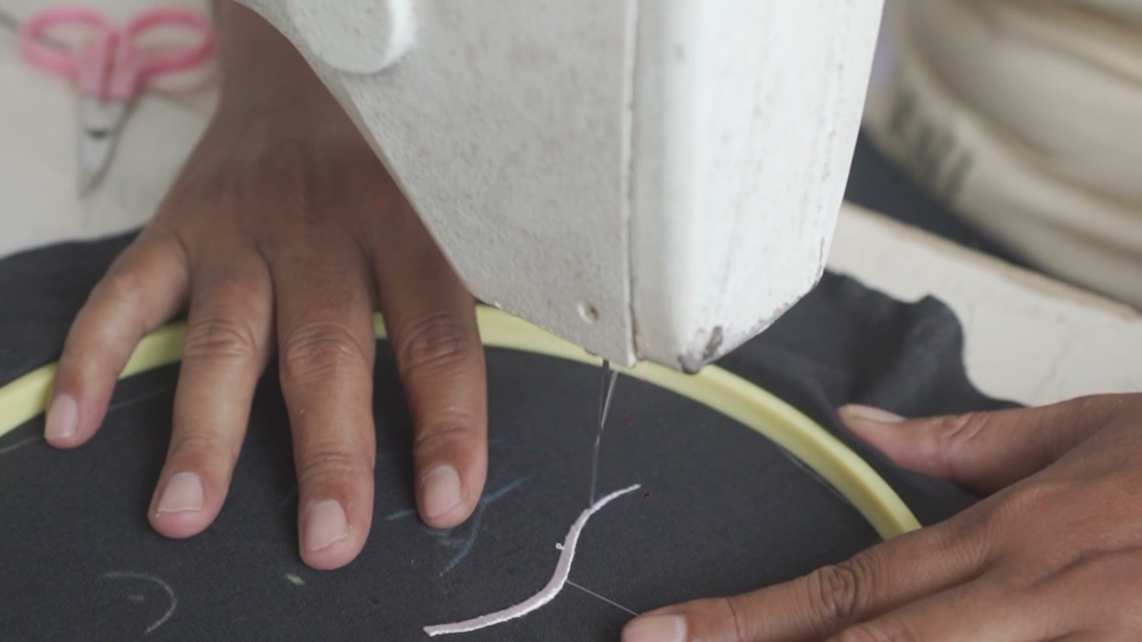 Hands guiding cloth in an embroidery hoop beneath the machine needle