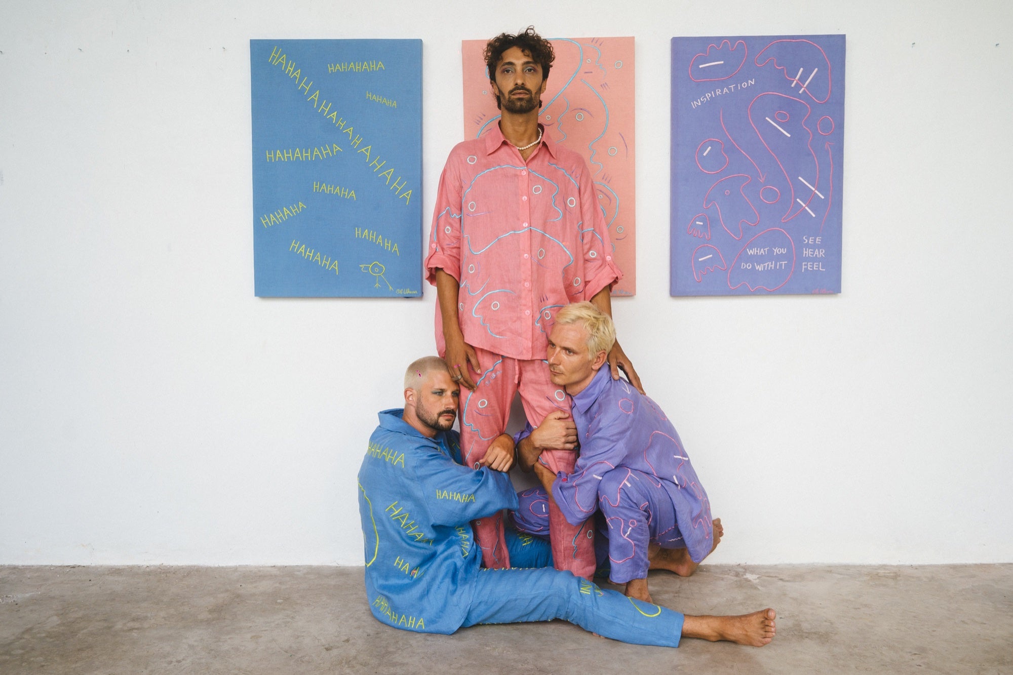 Three people wearing blue, pink and lilac Soft Code linen works beside paintings