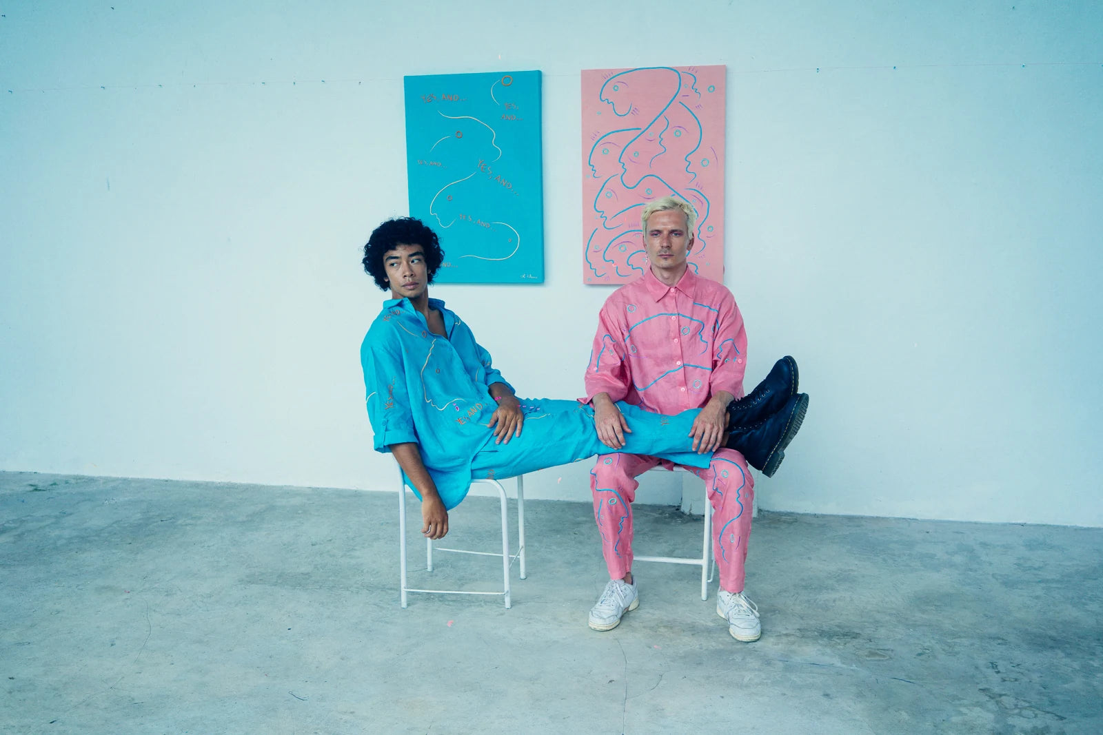 Two people in turquoise and pink linen beside related wall works